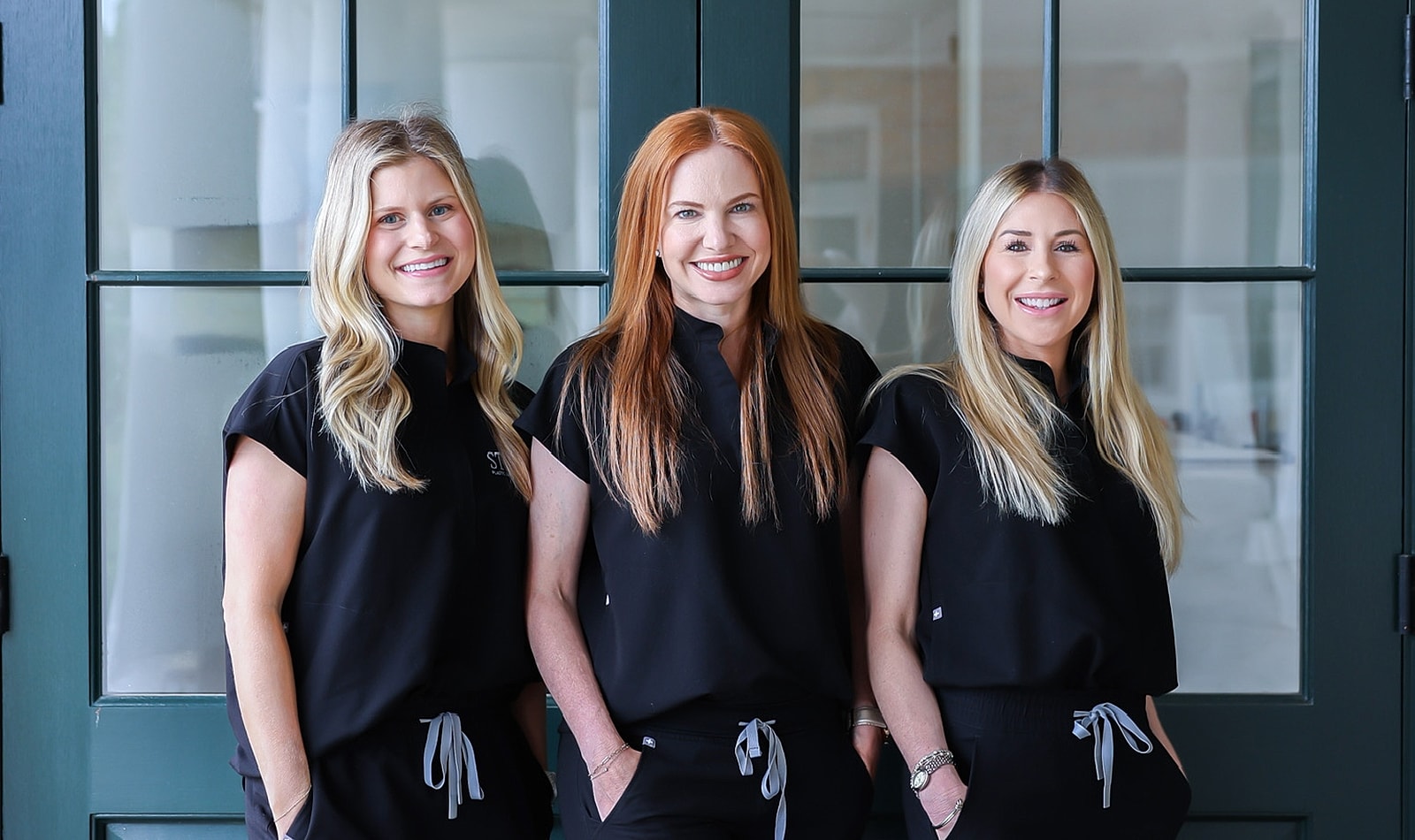 Three smiling women in matching black outfits.
